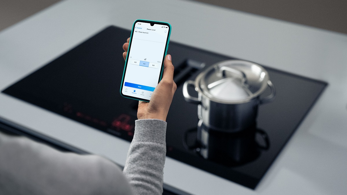 Osoba trzyma smartfon z aplikacją Home Connect obok płyty indukcyjnej z garnkiem.